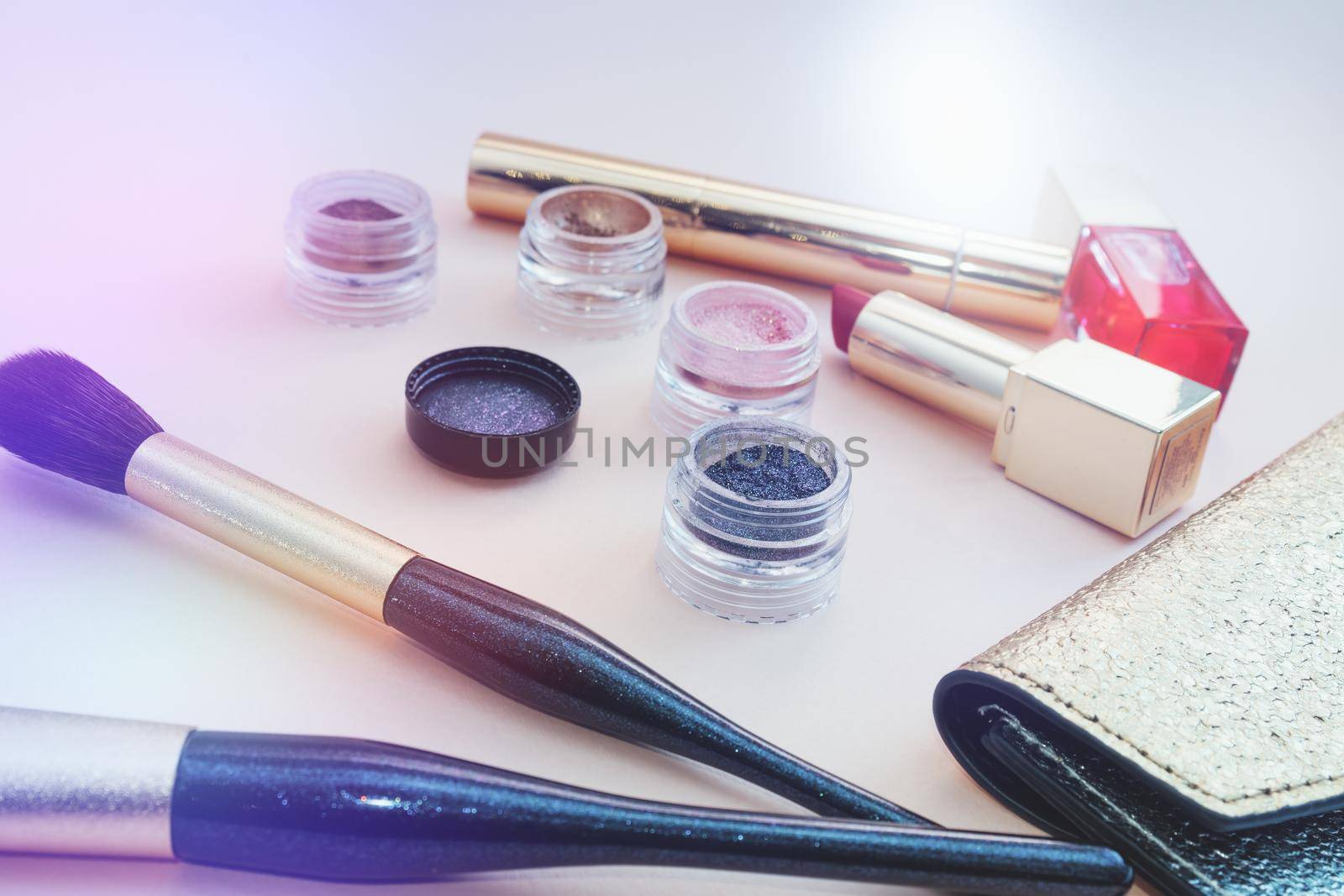 Top view of cosmetics standing out from golden makeup bag on pink background. Photo