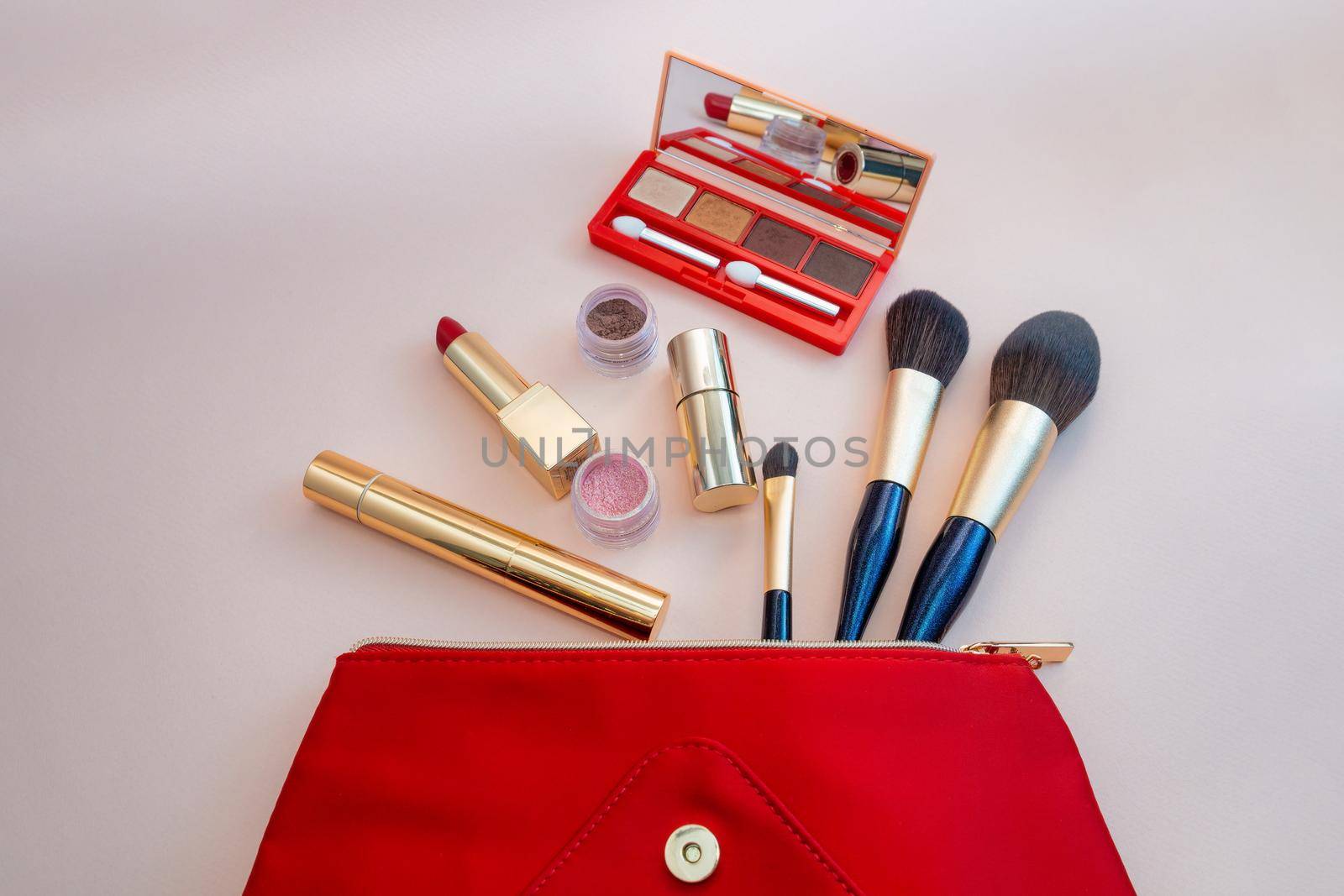 Top view of cosmetics standing out from red cosmetic bag on pink background by Andre1ns