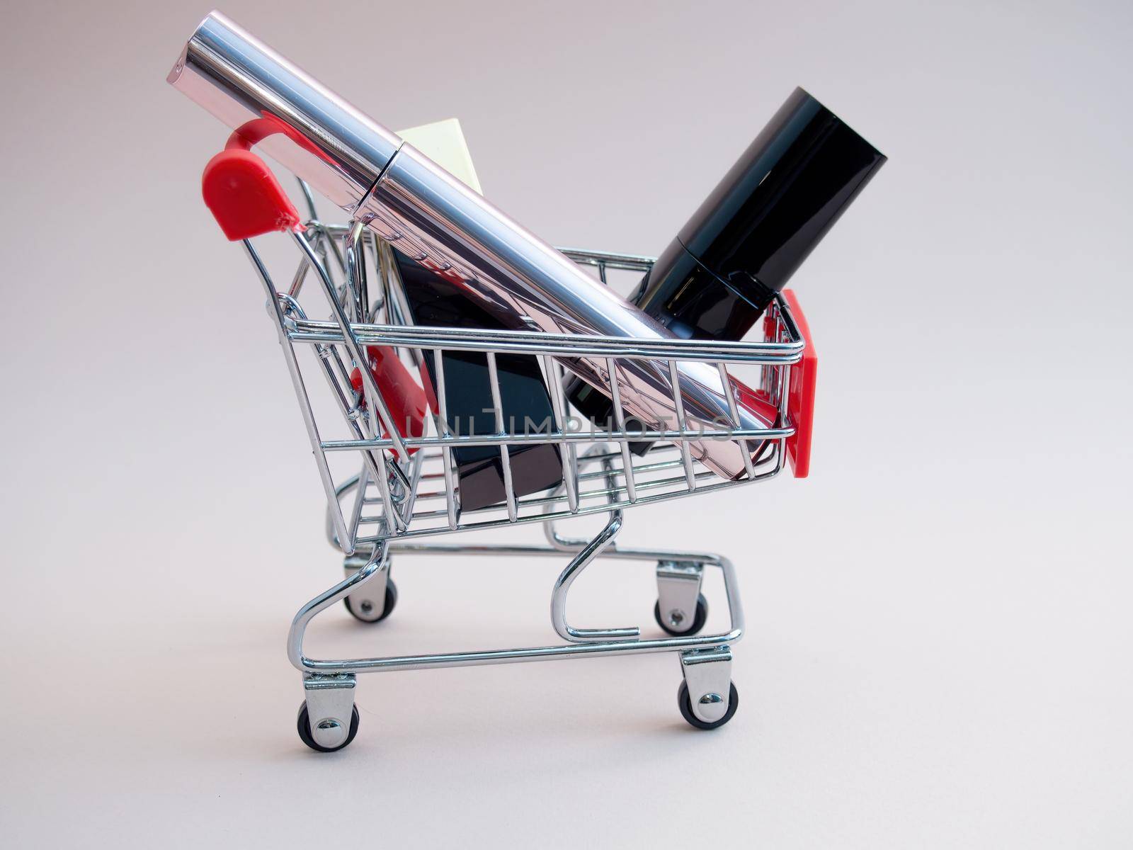 Front view of a shopping cart with makeup products on a pink background. Cosmetic shopping concept. photo