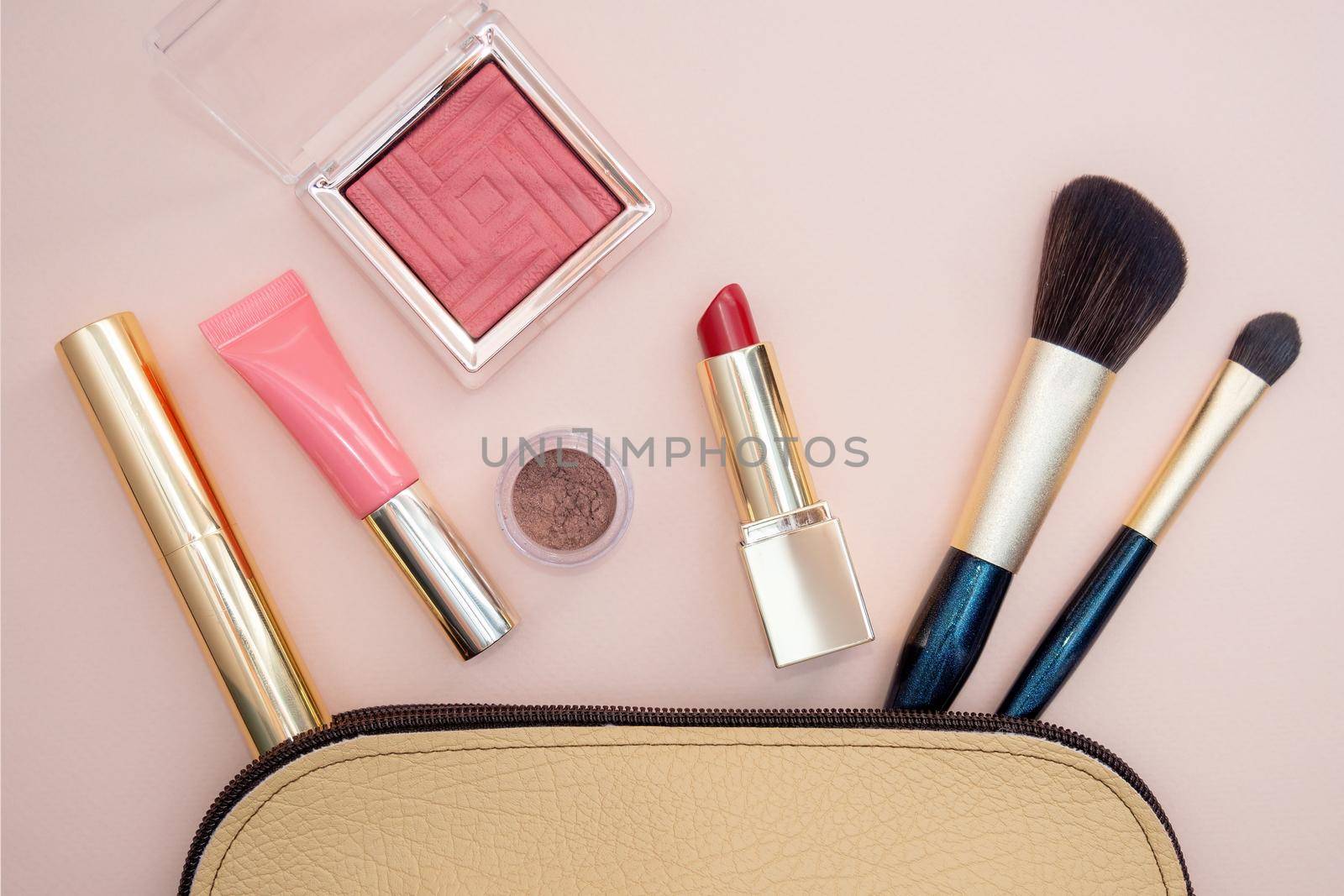 Top view of cosmetics standing out from beige makeup bag on pink background by Andre1ns