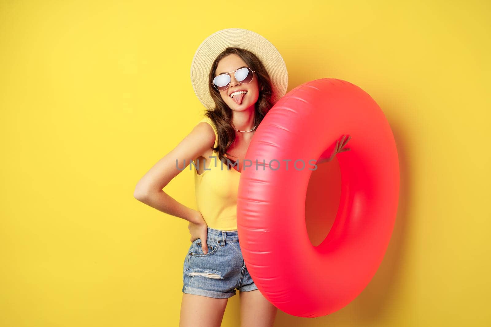 Stylish beach girl with swimming ring, laughing and smiling on summer vacation, sea trip, standing happy against yellow background.