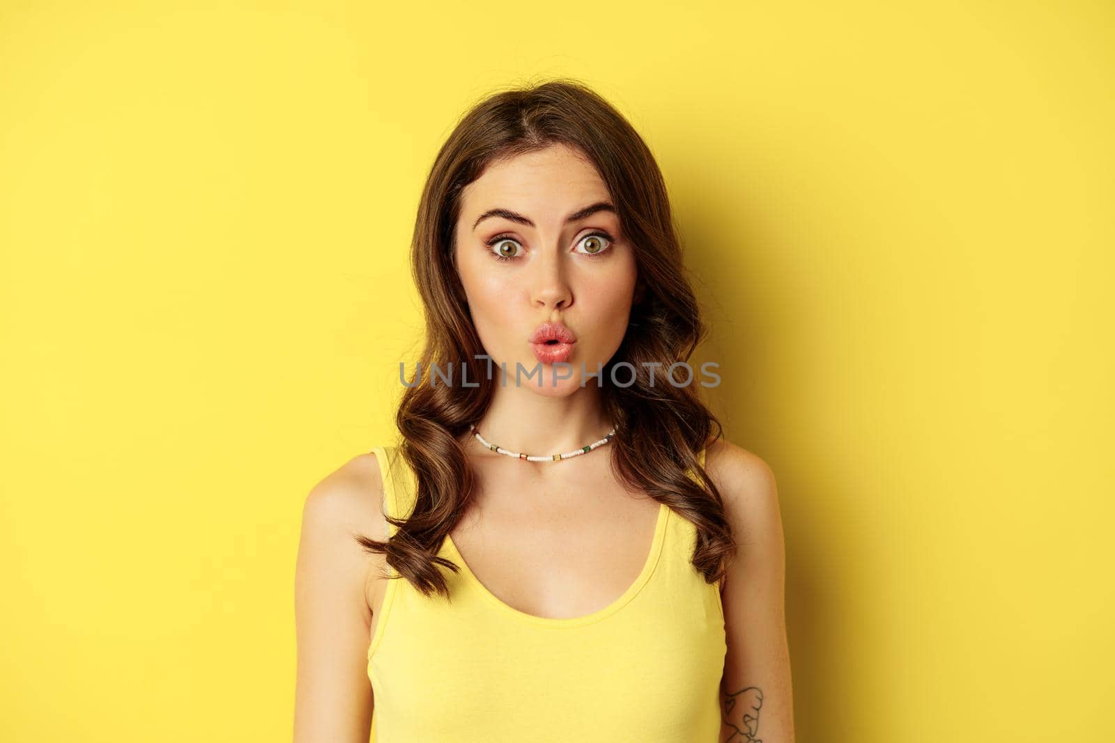 Close up portrait of stylish brunette girl looking amazed, wow face, showing excitement and surprise, impressed by something, standing over yellow background by Benzoix