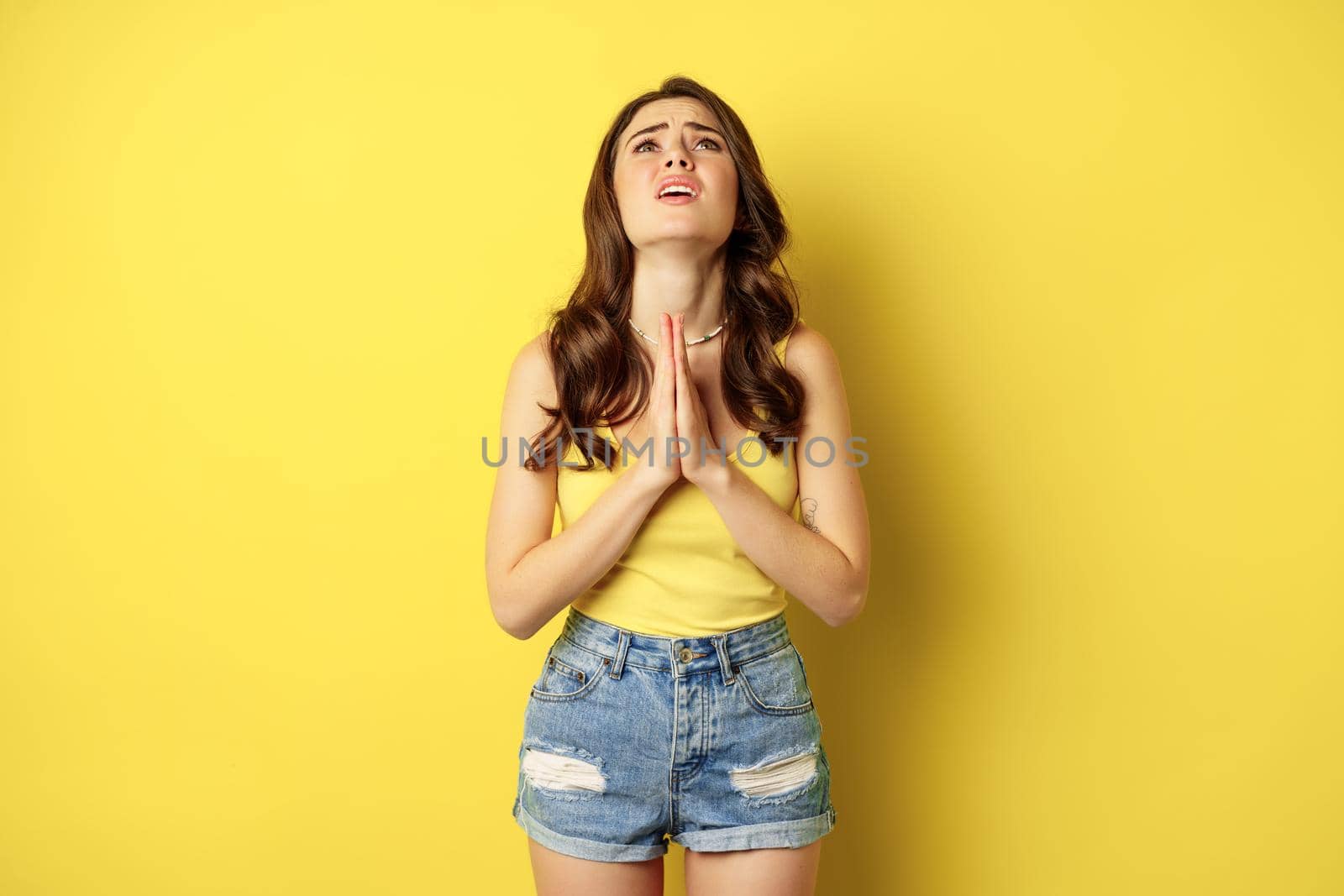 Desperate sad woman asking for help, begging with pray, need something, supplicating or praying, standing over yellow background. copy space
