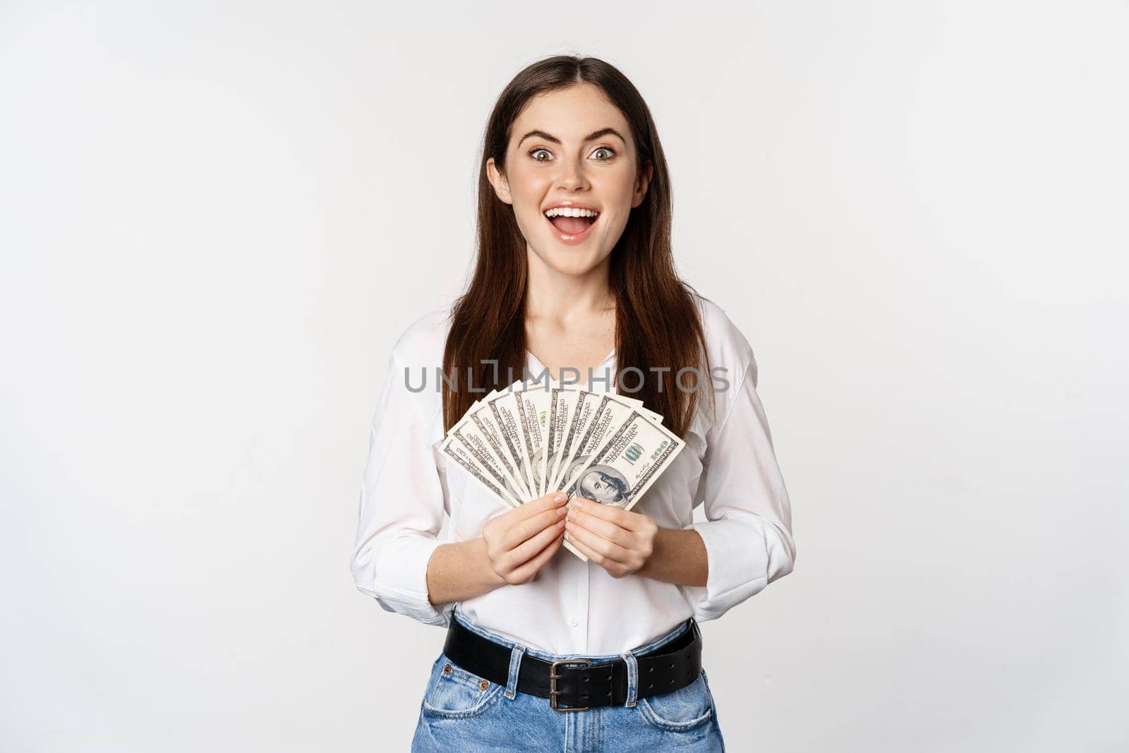 Portrait of beautiful woman holding money, cash, smiling pleased, standing over white background. Copy space