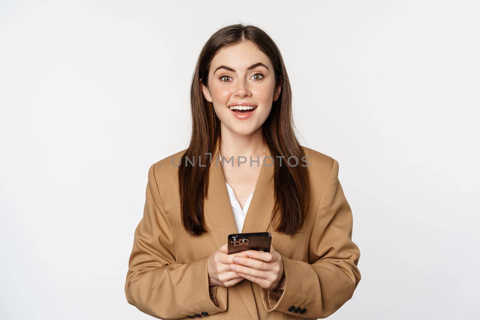 Smiling businesswoman using smartphone, app on mobile phone, standing over white background.