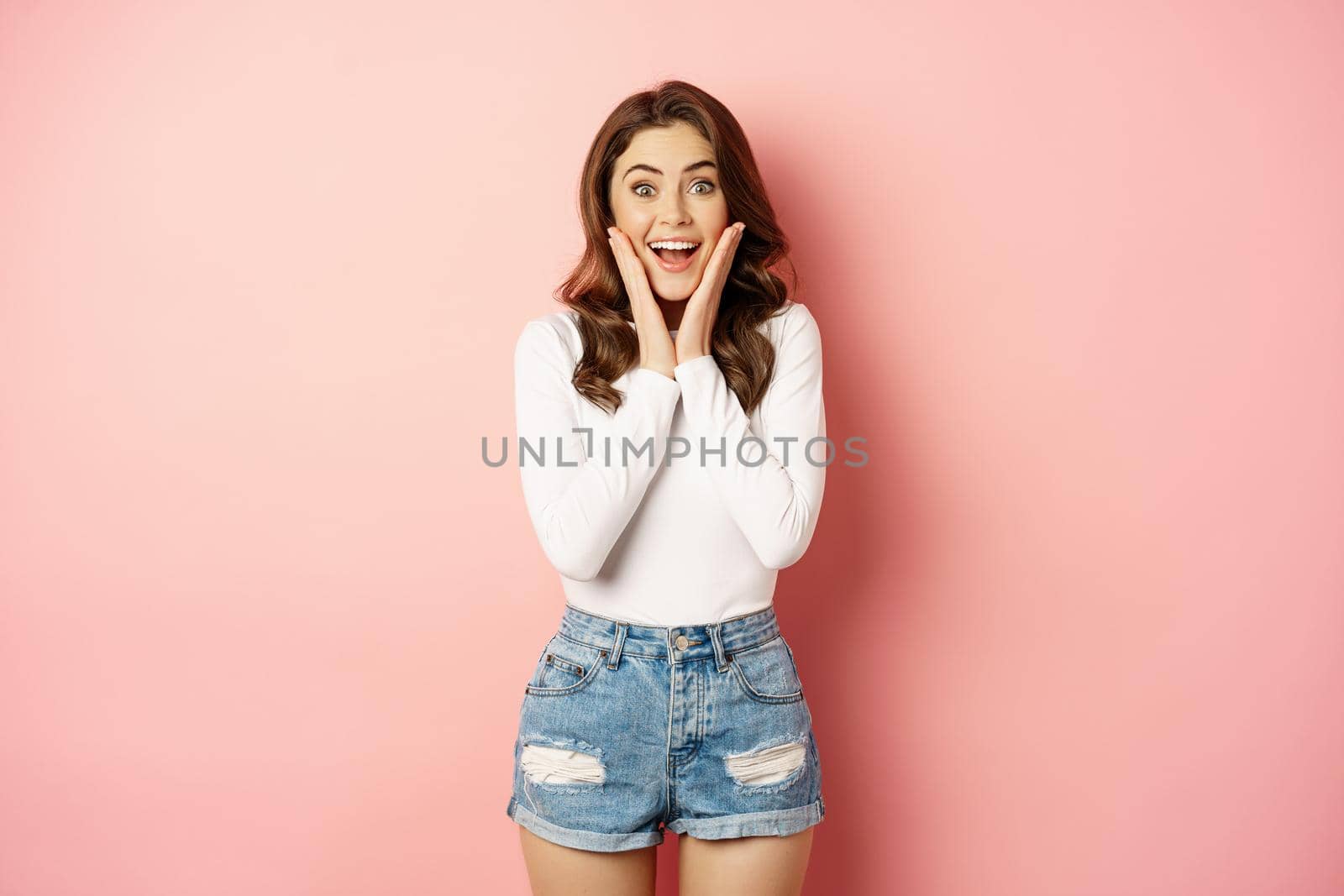 Happy attractive woman brunette smiling, looking with disbelief and excitement, winning, celebrating, reaction to great good news, pink background.