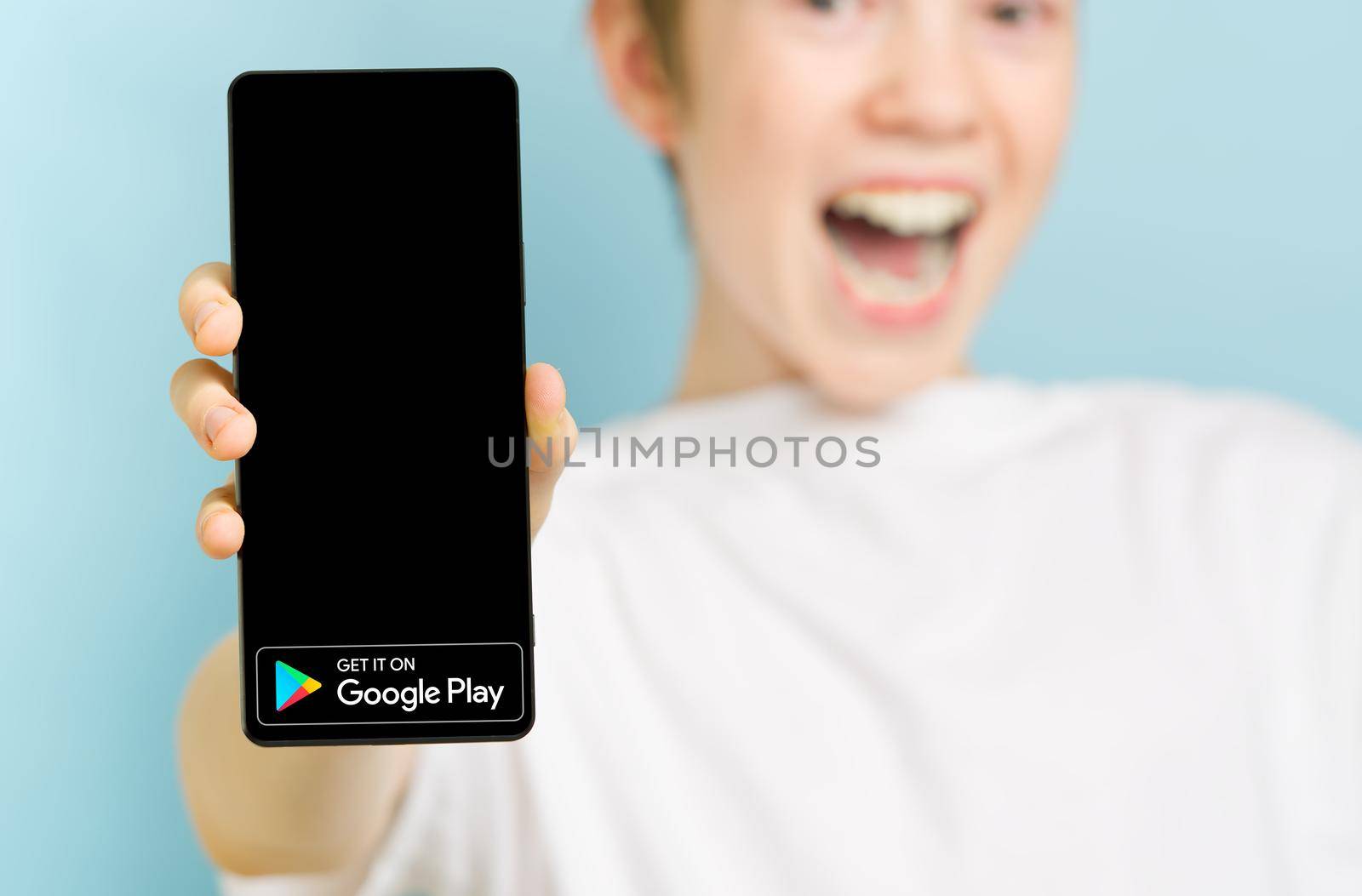 February 2022 - Tallinn, Estonia. Unfocused happy smiling boy with smartphone showing Google play market app logo. Social media