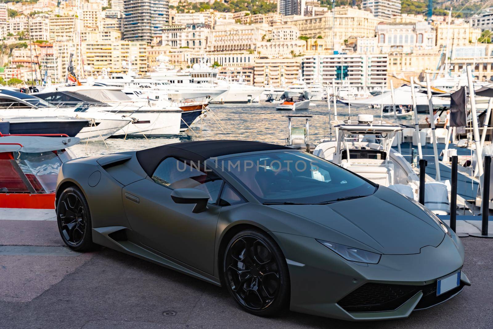 Luxury sport car of dark color is in port Hercules of Monaco in shadow, Monte-Carlo, very aggressive view of roadster, cabriolet, a lot of boats and yachts are on background. High quality photo