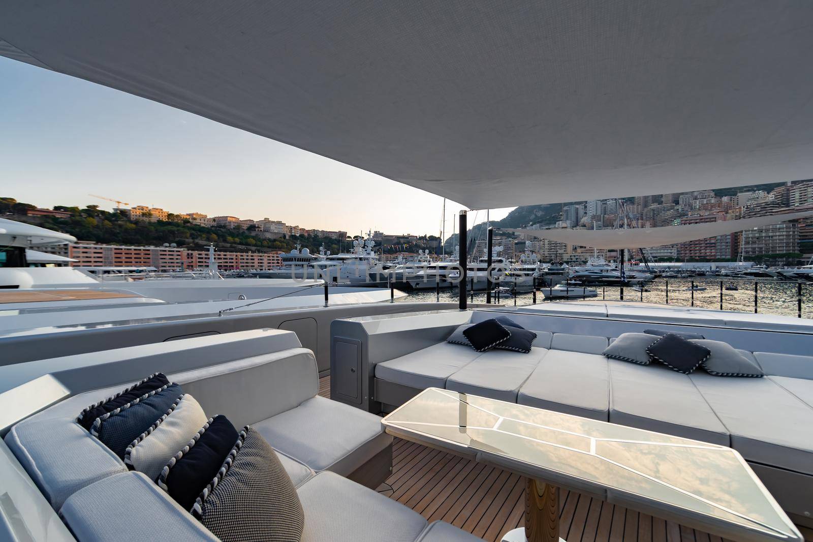 The front deck of huge yacht in port of Monaco at sunset, the place for landing of helicopter, a lot of motorboats are on background, the chrome plated handrail, megayacht is moored in marina, dusk. High quality photo