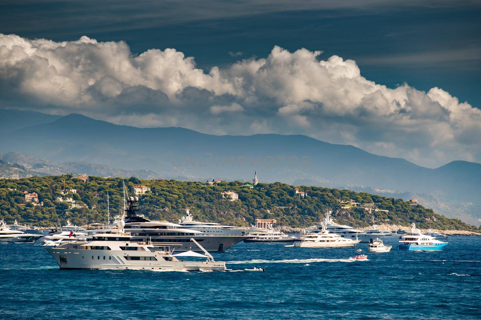 A lot of huge yachts are in harbour near port Hercules of Monaco at sunny day, megayachts are moored in sea, is a yacht show, Monte Carlo, island is on background, glossy board of the megayachts. High quality photo