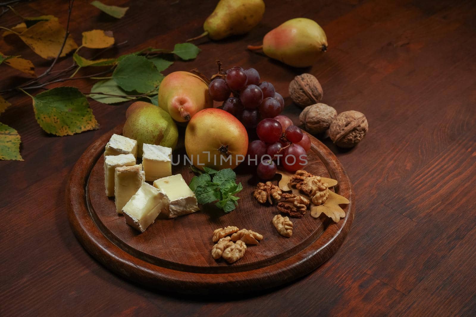 Best wine snacks set: cheese, grapes, pear and three walnuts on a wooden table. Brie cheese with fruits, grapes, walnuts on a dark wooden plate and wooden board.