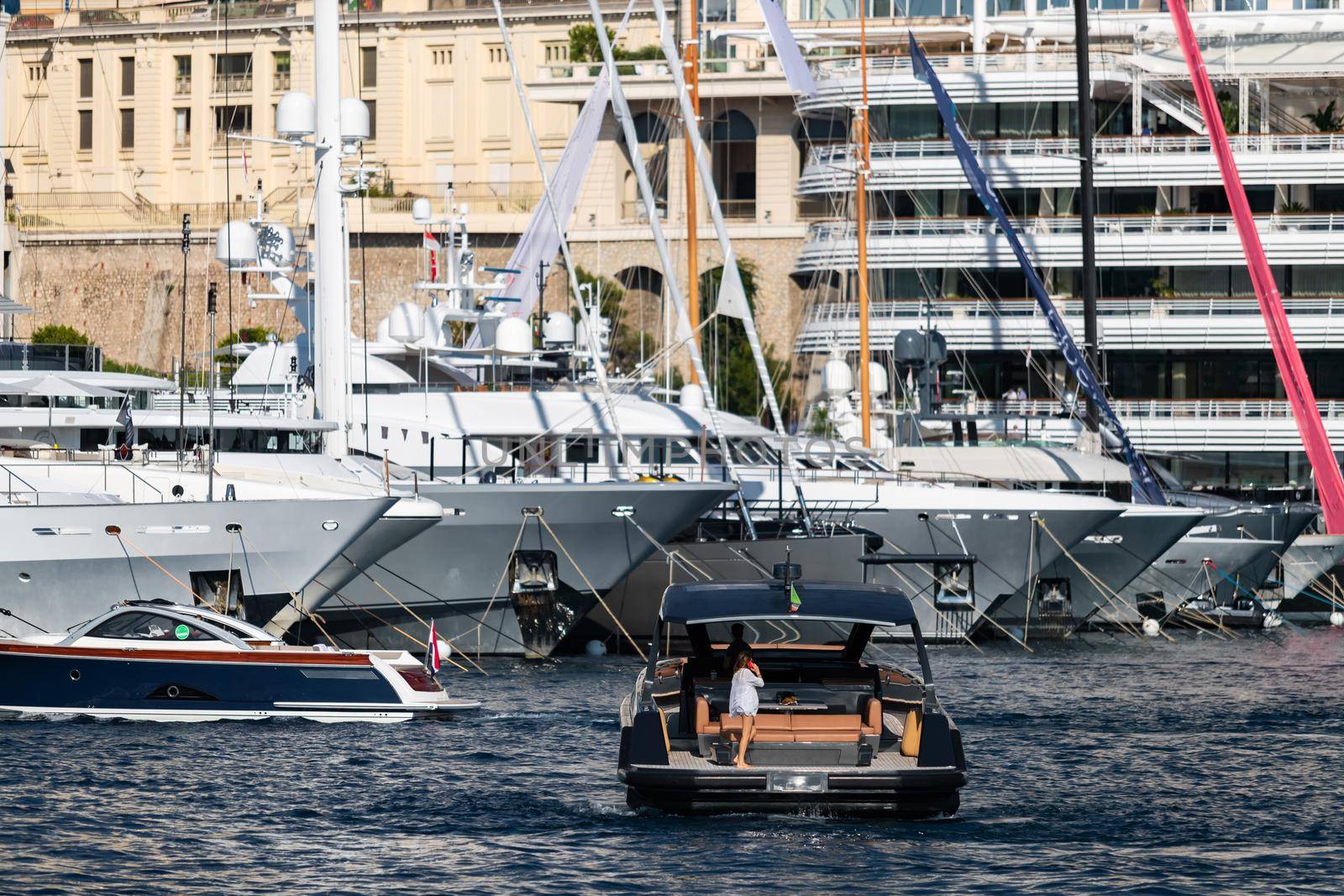 A large boat enters the port, the girl on the deck is talking on the phone, A lot of huge yachts are in port of Monaco on background, Monte Carlo, megayachts are moored in marina, sun reflection. High quality photo