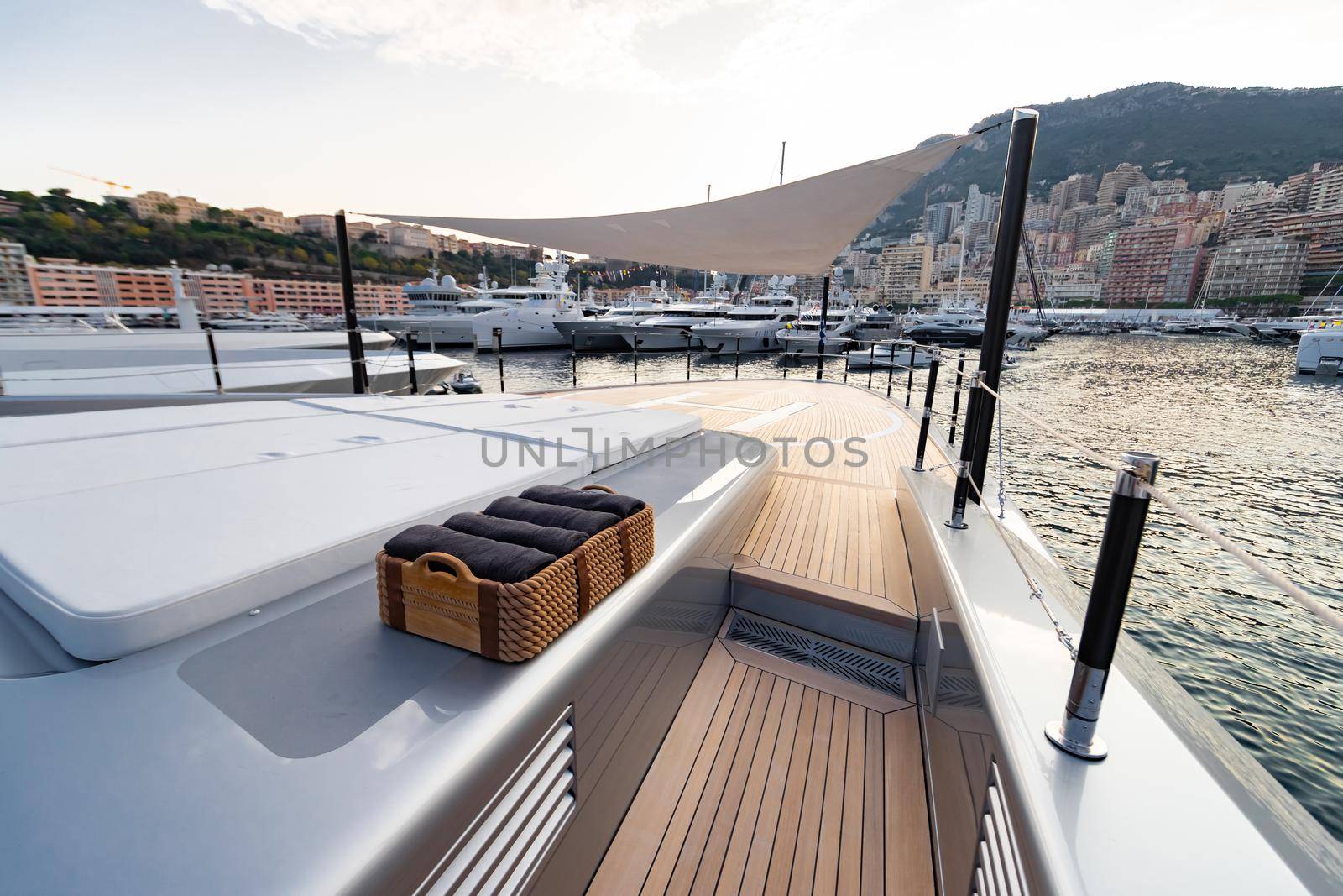 The front deck of huge yacht in port of Monaco at sunset, the place for landing of helicopter, a lot of motorboats are on background, the chrome plated handrail, megayacht is moored in marina, dusk. High quality photo