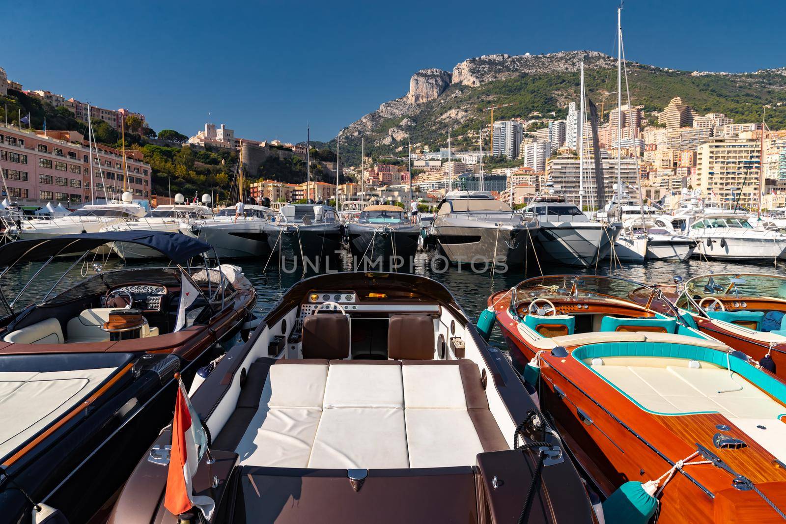 A lot of motor boats in rows are in port of Monaco at sunny day, Monte Carlo, mountain is on background, colourful interior of the boat, are moored in marina, sun reflection on glossy board. High quality photo