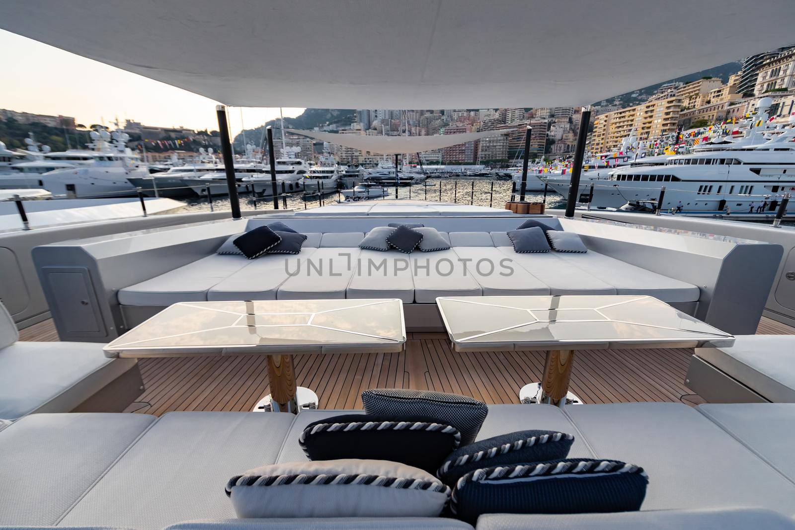 The front deck of huge yacht in port of Monaco at sunset, the place for landing of helicopter, a lot of motorboats are on background, the chrome plated handrail, megayacht is moored in marina, dusk. High quality photo