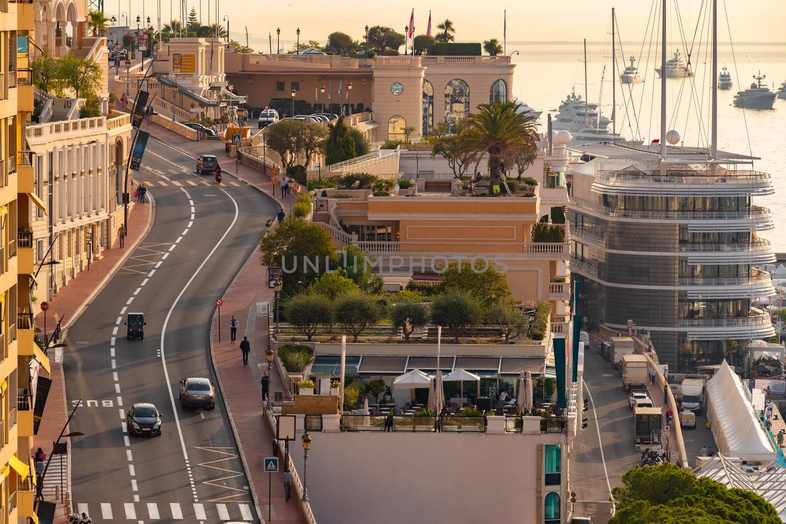 Cityscape of the main street along the port of Hercules in the Principality of Monaco in the morning, Monte-Carlo, few cars and people, huge motor yachts standing at sea, soft yellow sunrise light. High quality photo