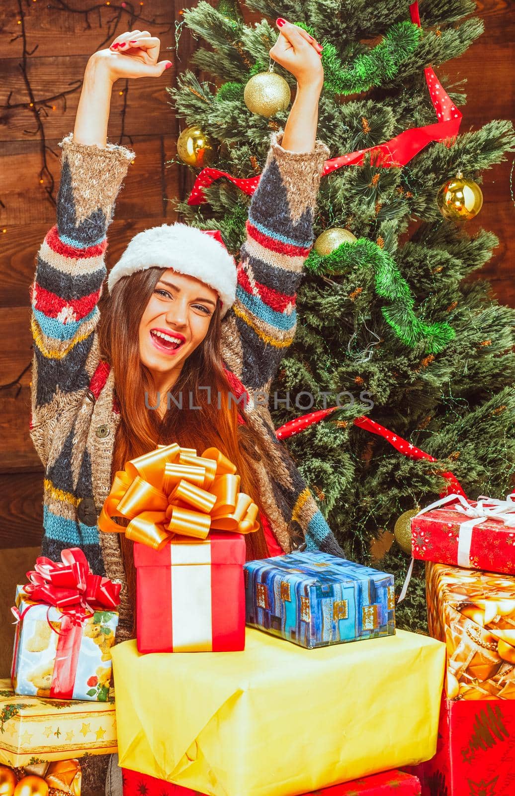 Happy Young Woman in a Santa Hat among the Mountain of Gifts on the Background of a Decorated Christmas Tree. Wood background. Close-up. High quality photo