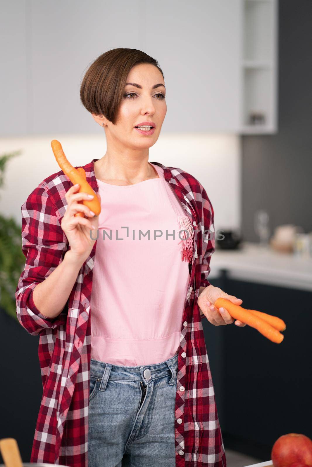 Pretty housewife with fresh carrot in the hands with a short hairstyle prepares carrot cake in the kitchen. Healthy food at home. Healthy food leaving concept.