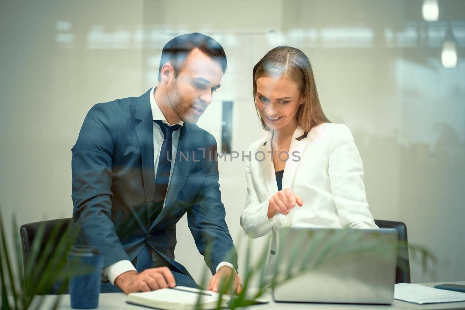 Handsome young businessman and a woman working on laptop in the office. Smiling diverse business partners young man and woman discussing project sitting in a modern bright meeting.
