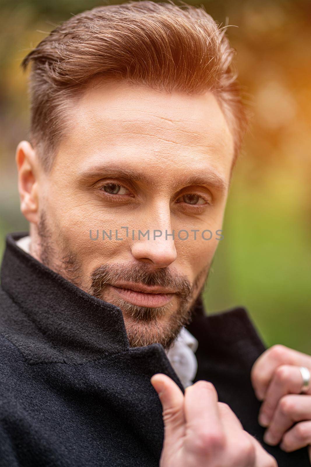 Handsome man holding a corner of his coat standing on the street in an autumn coat smiling looking at the camera. Handsome young man in dark blue coat and scarf or muffler.