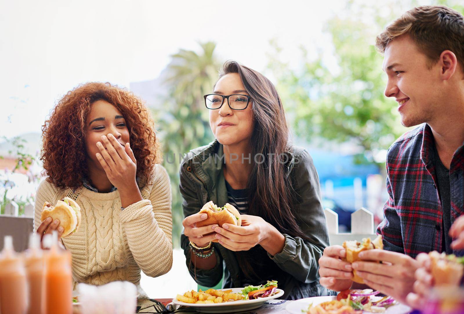 Cropped shot of three friends eating burgers outdoors