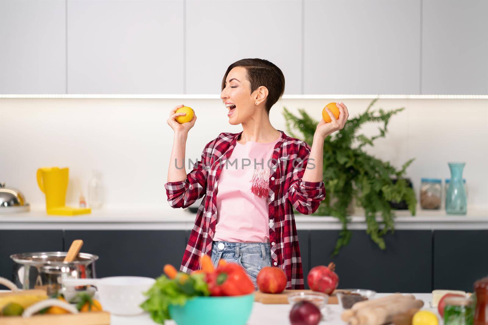 Happy mother with fresh yellow tomatoes in hands wearing plaid shirt with a short hairstyle cooking in the kitchen. Healthy food at home. Healthy food leaving concept.