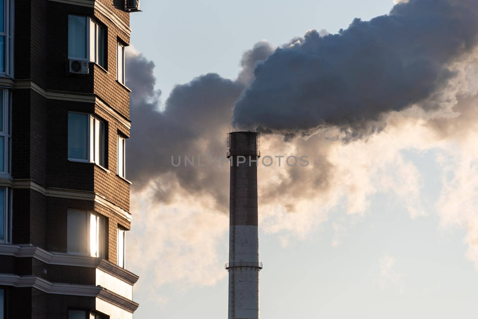 Pipe of combined heat and power plant CHP against background of multi-storey residential buildings.