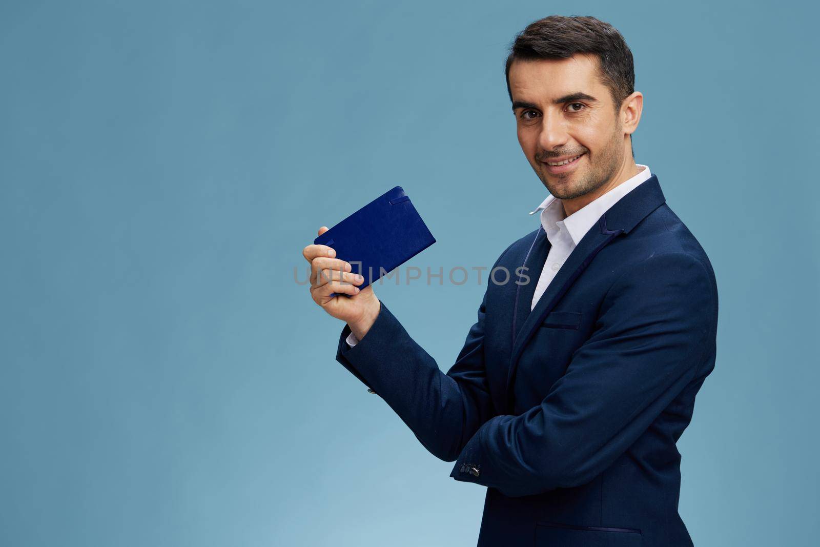 smiling man with notepad in hand in a stylish suit posing self-confidence blue background. High quality photo