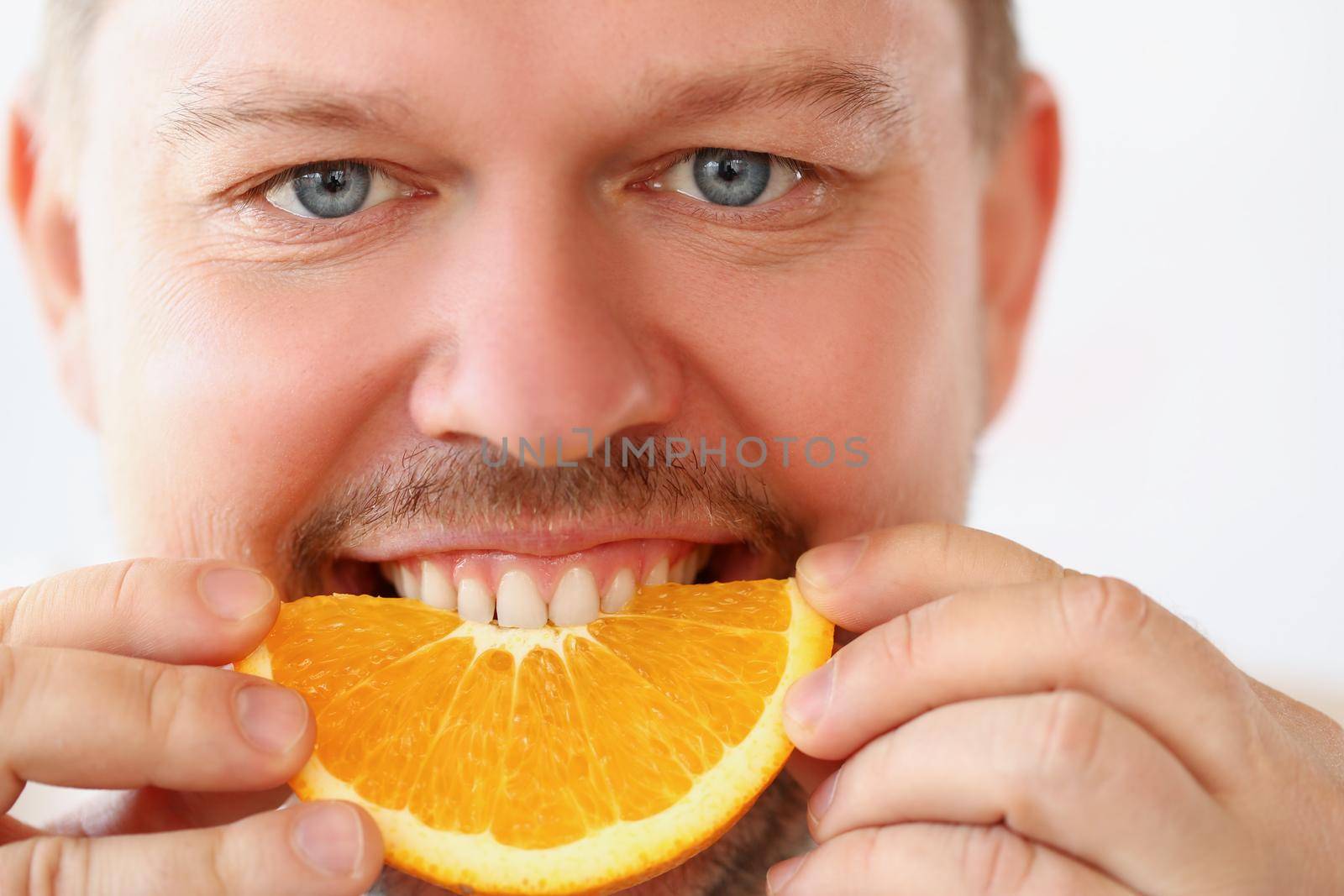 Close-up of man bite chopped slice of orange for breakfast in kitchen, healthy eating, strict diet, juicy, fruit, summer harvest, vitaminized snack concept