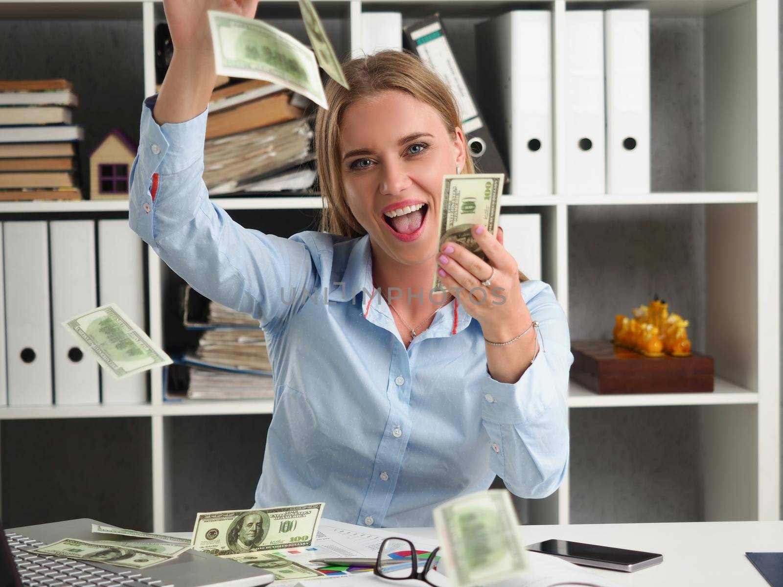 Cheerful woman throw in air dollars banknotes at work, cash everywhere in office by kuprevich