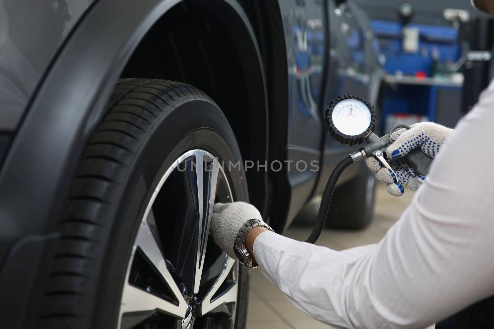 Close-up of automechanic pumping up tires with special instrument at work. Qualified worker fix machine on station. Car maintenance, repair service concept