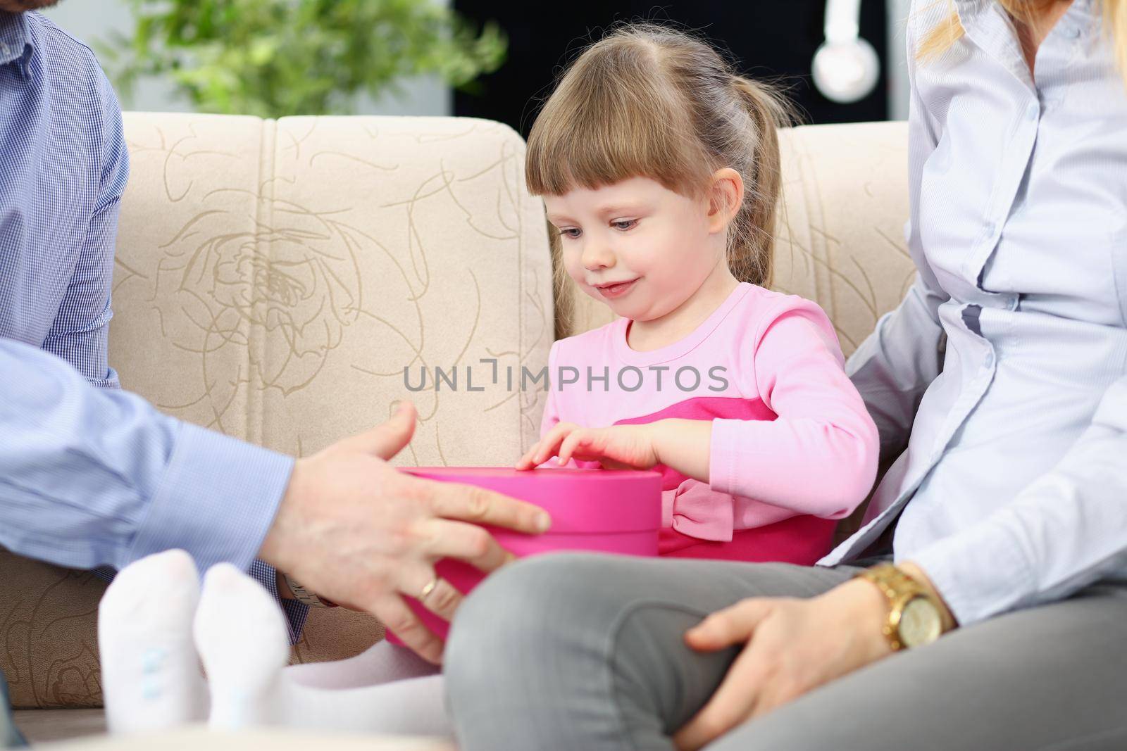 Portrait of parents give present to their little daughter, pink box with surprise inside. Warm and happy moment in family, cute kid. Birthday, gift concept