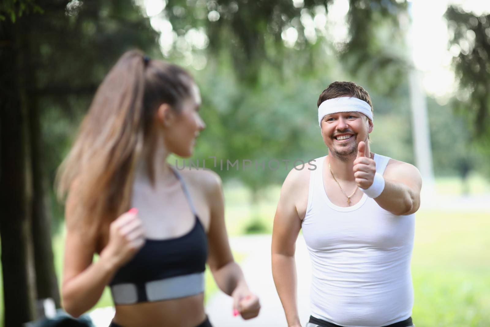 Portrait of tired middle aged man running in early morning with woman friend. Active woman jogging in front, feeling energetic. Weight loss, health concept