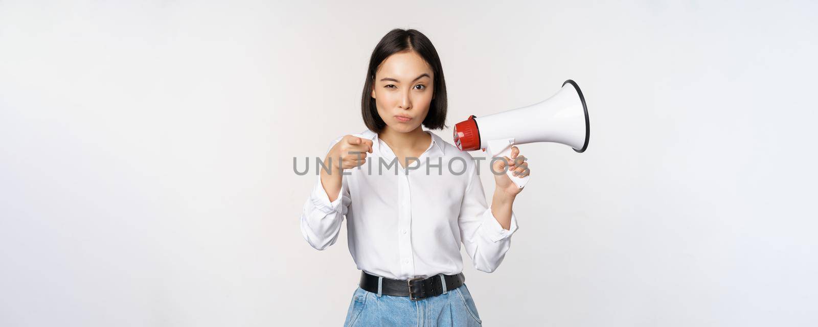 Image of modern asian woman with megaphone, pointing at you camera, making announcement, white background.