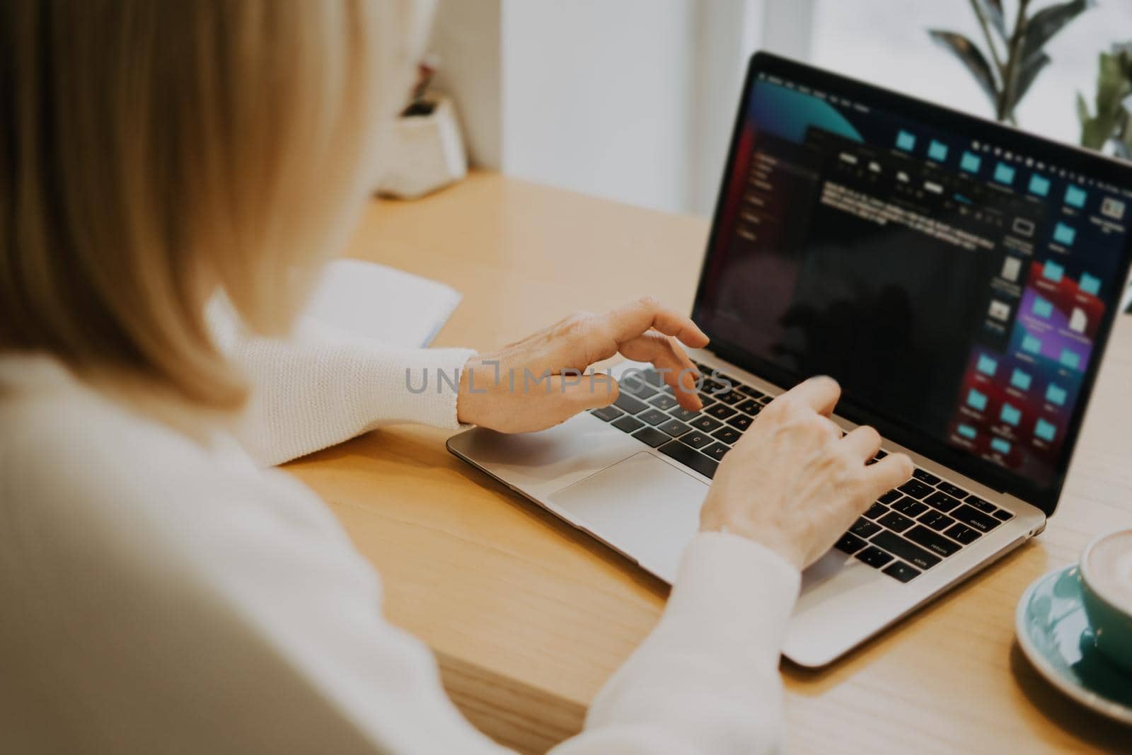 Mature adult woman hands, sitting in cafe with coffee mug and working online on laptop. Businesswoman typing on notebook computer in coworking space in roasters coffee shop, close up