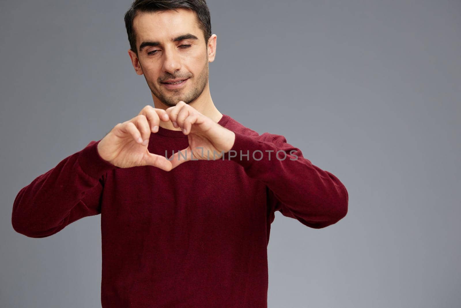 handsome man holding hands in the shape of a heart in a red sweater gesturing with hands posing. High quality photo