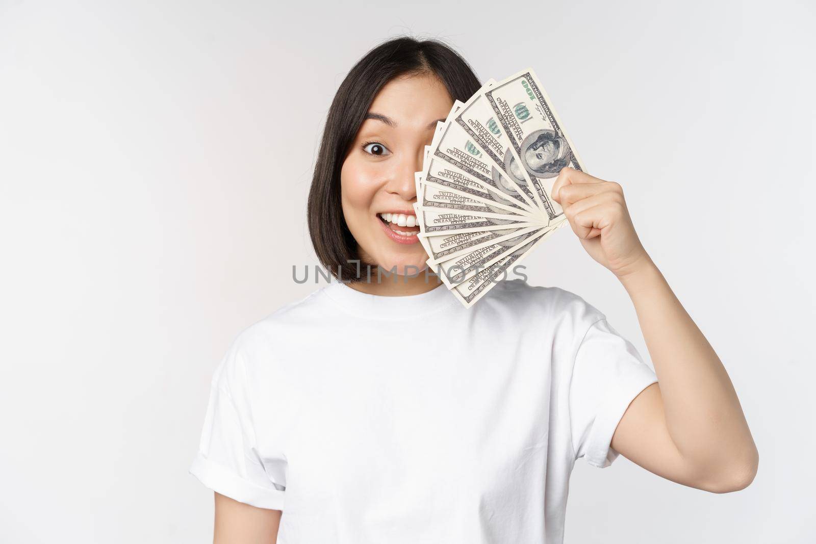 Portrait of smiling asian woman holding dollars money, concept of microcredit, finance and cash, standing over white background.