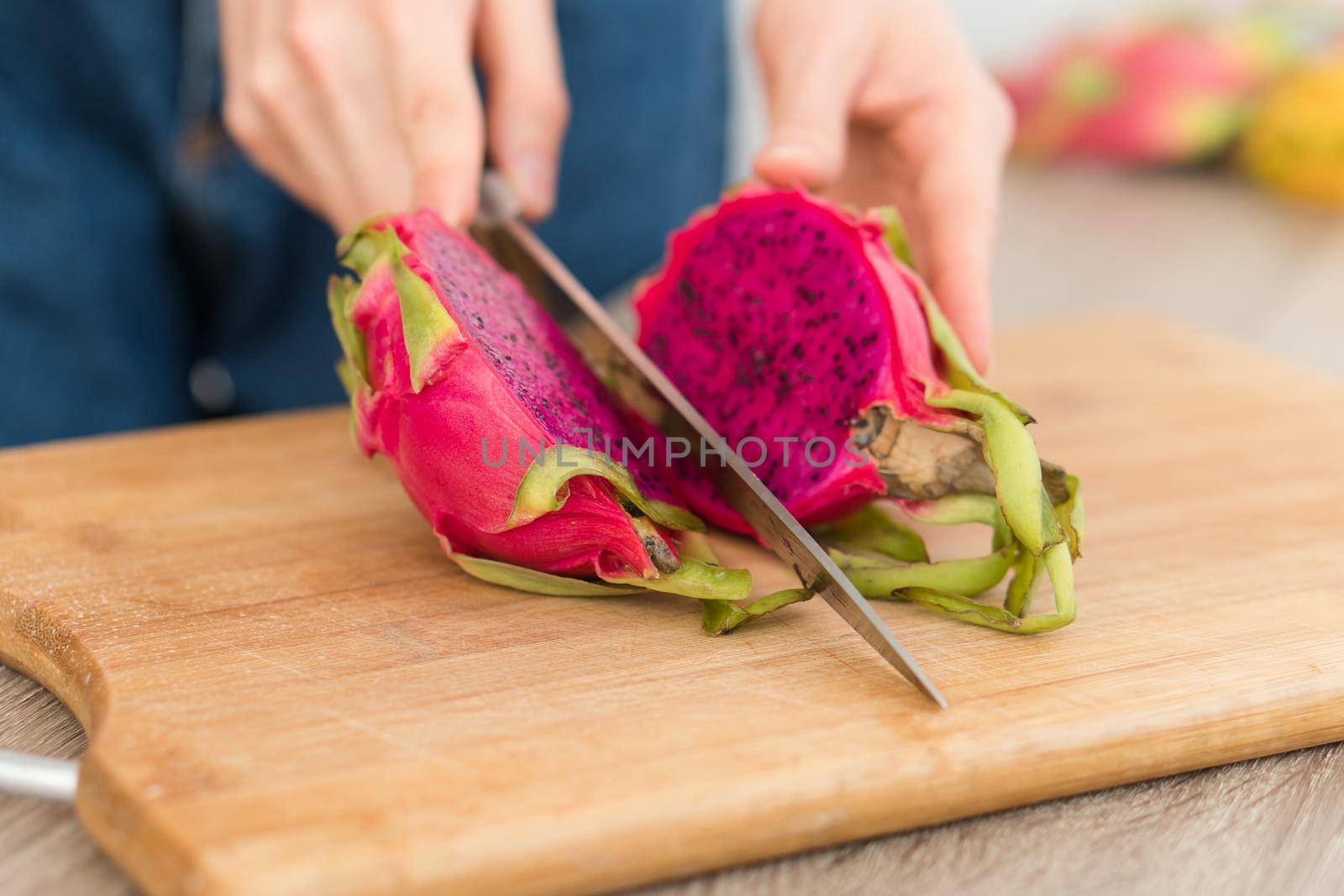 Female hands is cutting a dragon fruit or pitaya with pink skin and pulp with black seeds on wooden cut board on the table. Exotic fruits, healthy eating concept.