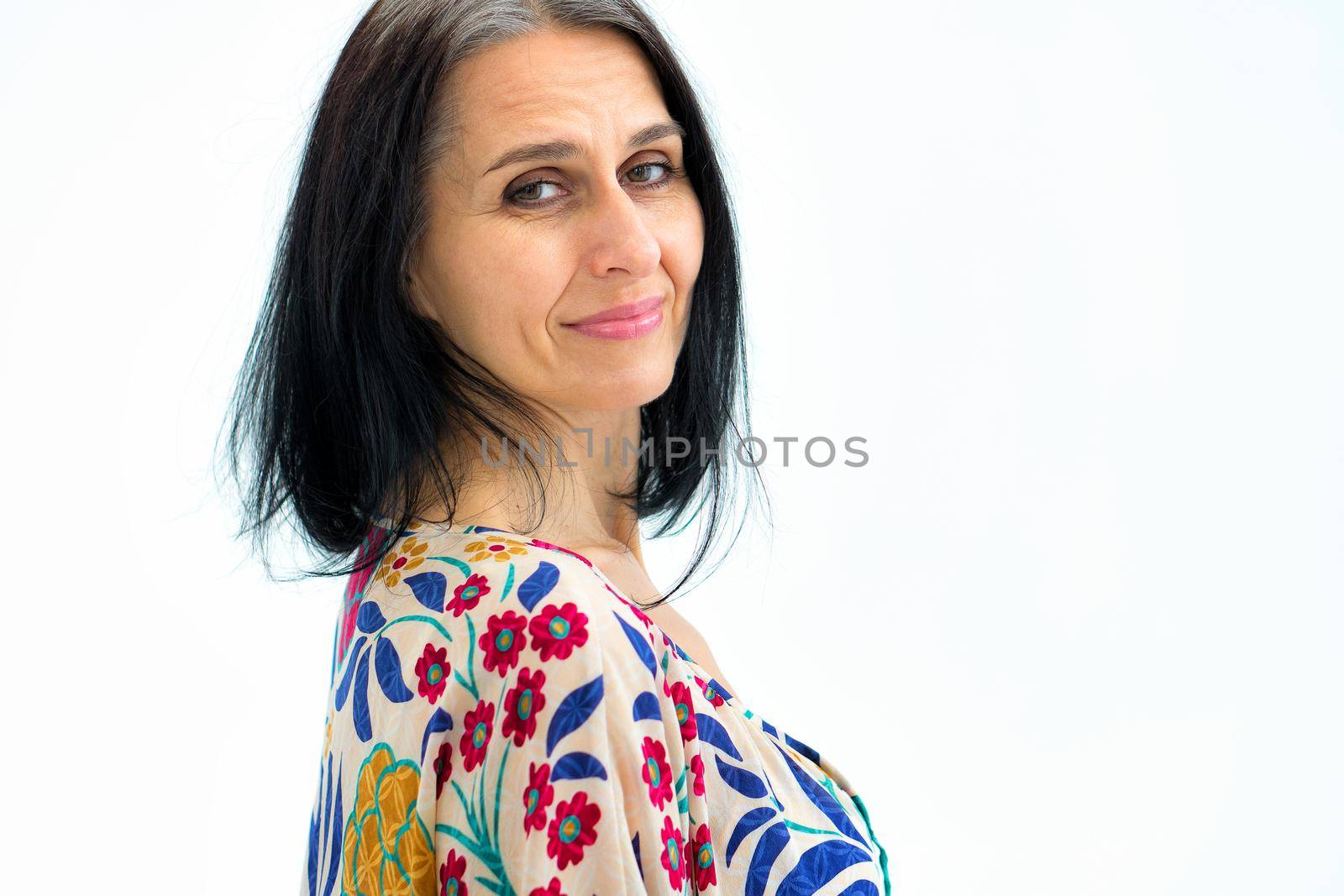 Close-up portrait of middle aged woman starting getting grey-haired wearing dress with flowers on white background, middle age sexy lady, cosmetology concept by balinska_lv