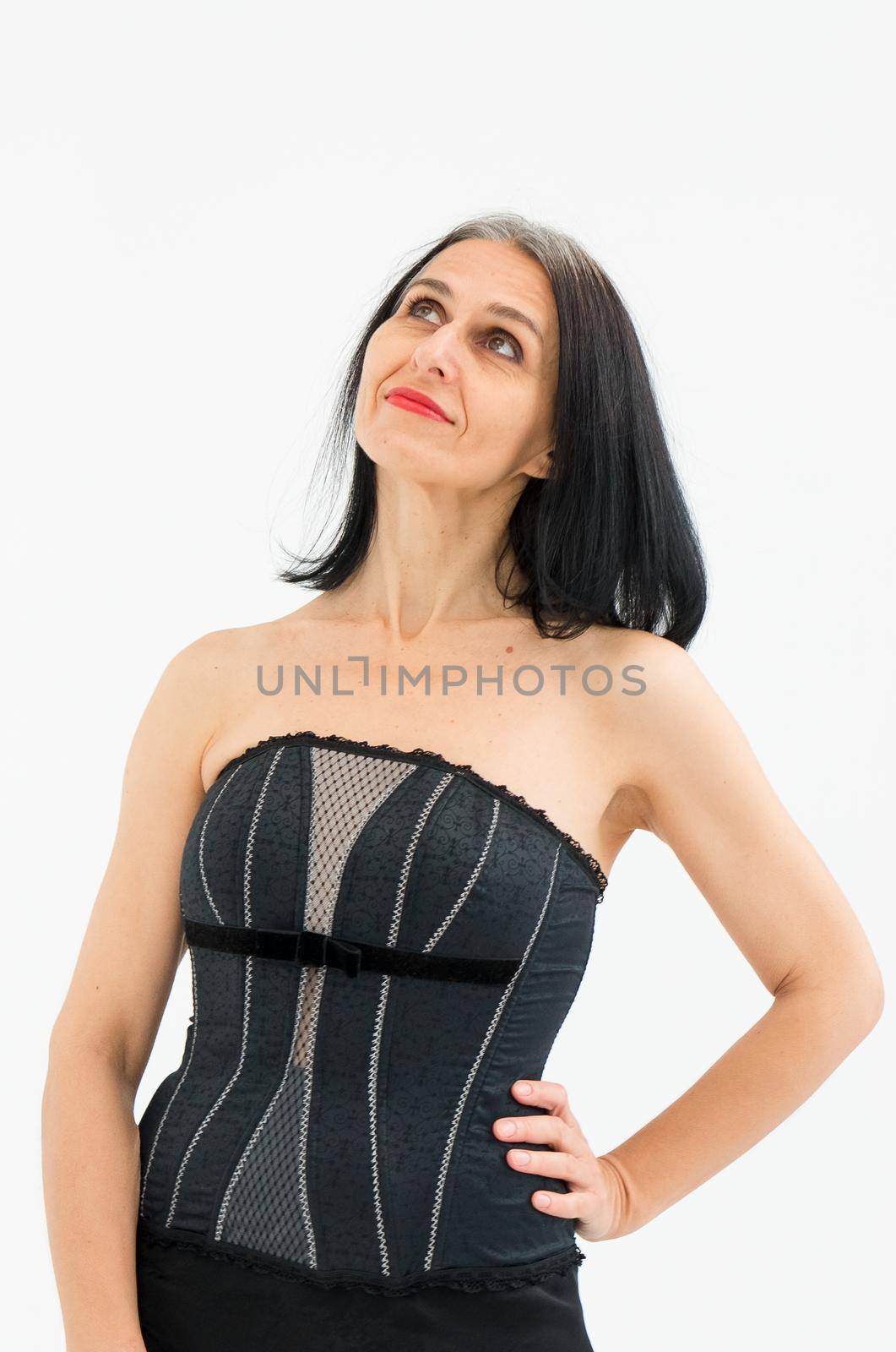 Middle aged woman starting getting grey-haired is posing in studio in black clothes and stockings on white background, middle age sexy lady, cosmetology concept.