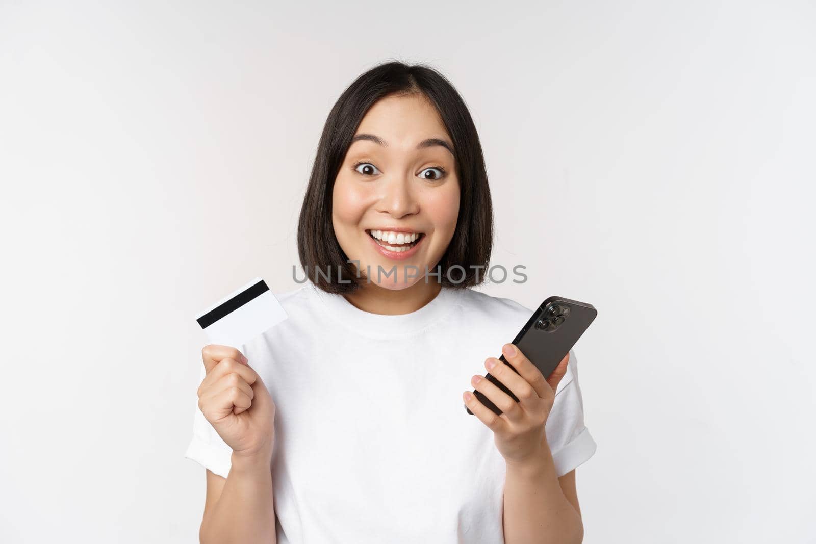 Online shopping. Happy asian woman using credit card and smartphone app, paying on website via mobile phone, white background.