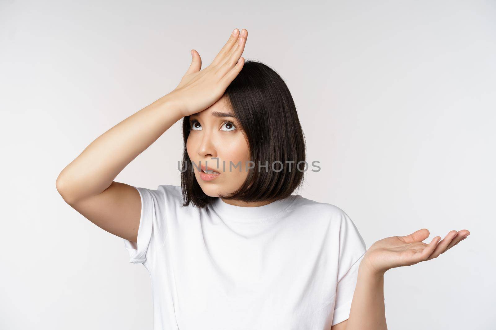 Annoyed korean girl facepalm, slap forehead and shrugging, confused by smth, standing over white background by Benzoix