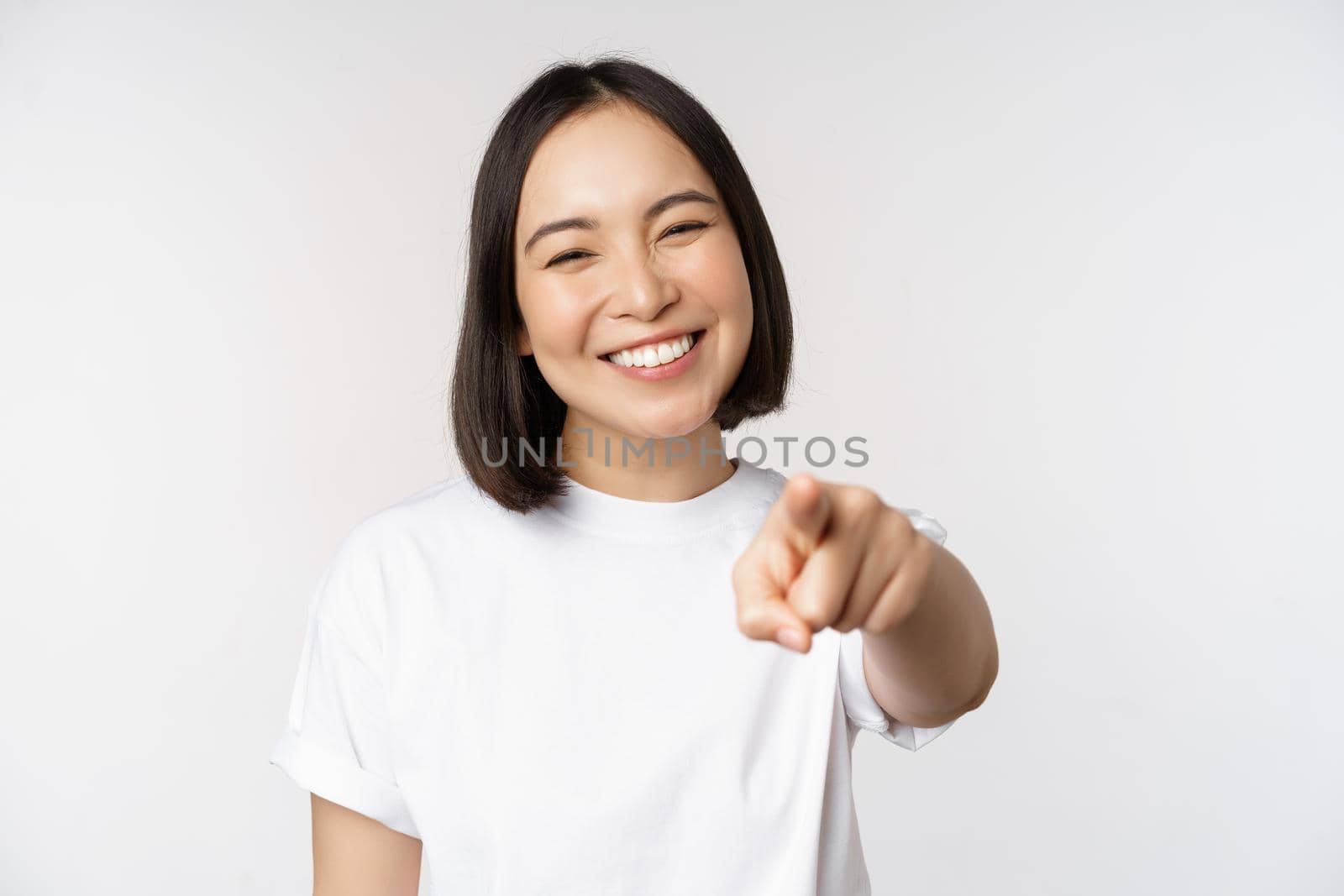 Portrait of happy smiling asian woman with white teeth, pointing finger at camera, choosing you, congratulating, standing over white background by Benzoix