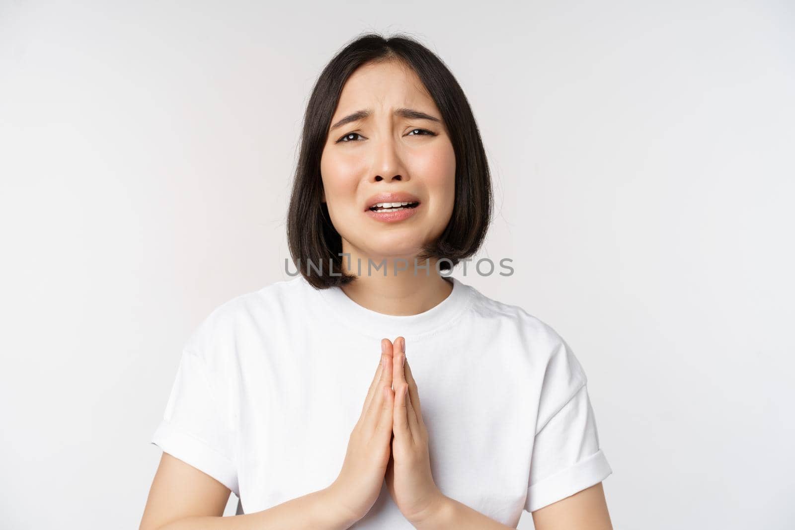 Desperate crying asian woman begging, asking for help, pleading and say please, standing in white t-shirt over white background by Benzoix