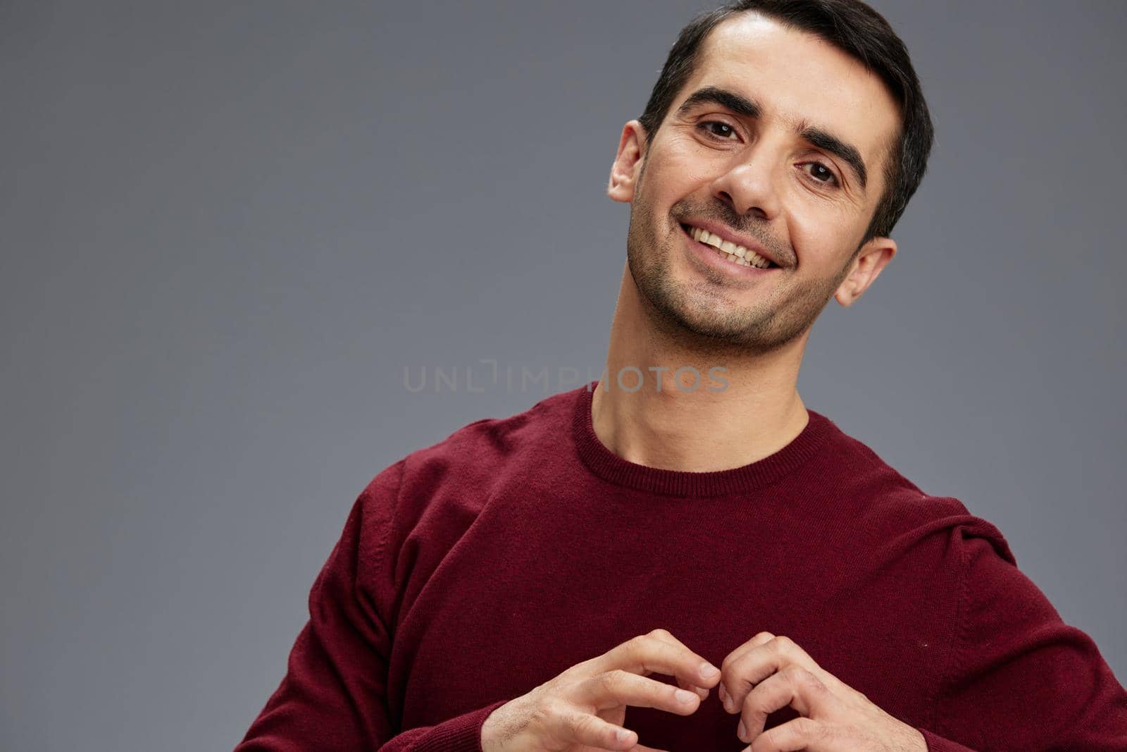 portrait of a smiling man in a red sweater gesturing with hands posing Gray background by SHOTPRIME