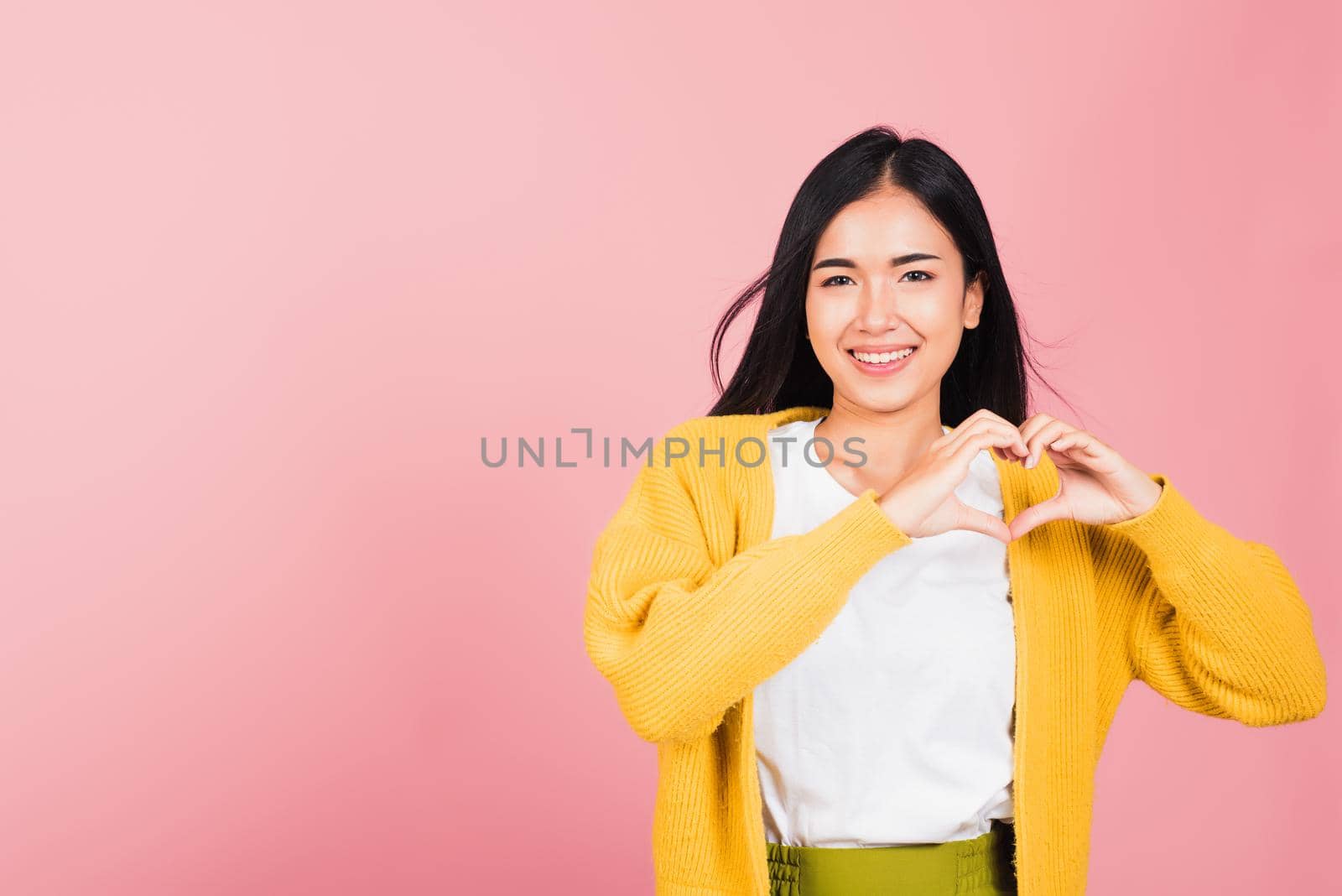 Happy Asian portrait beautiful cute young woman smile make finger heart gesture figure symbol shape sign with two hands sending love to her lover looking camera, studio shot isolated pink background