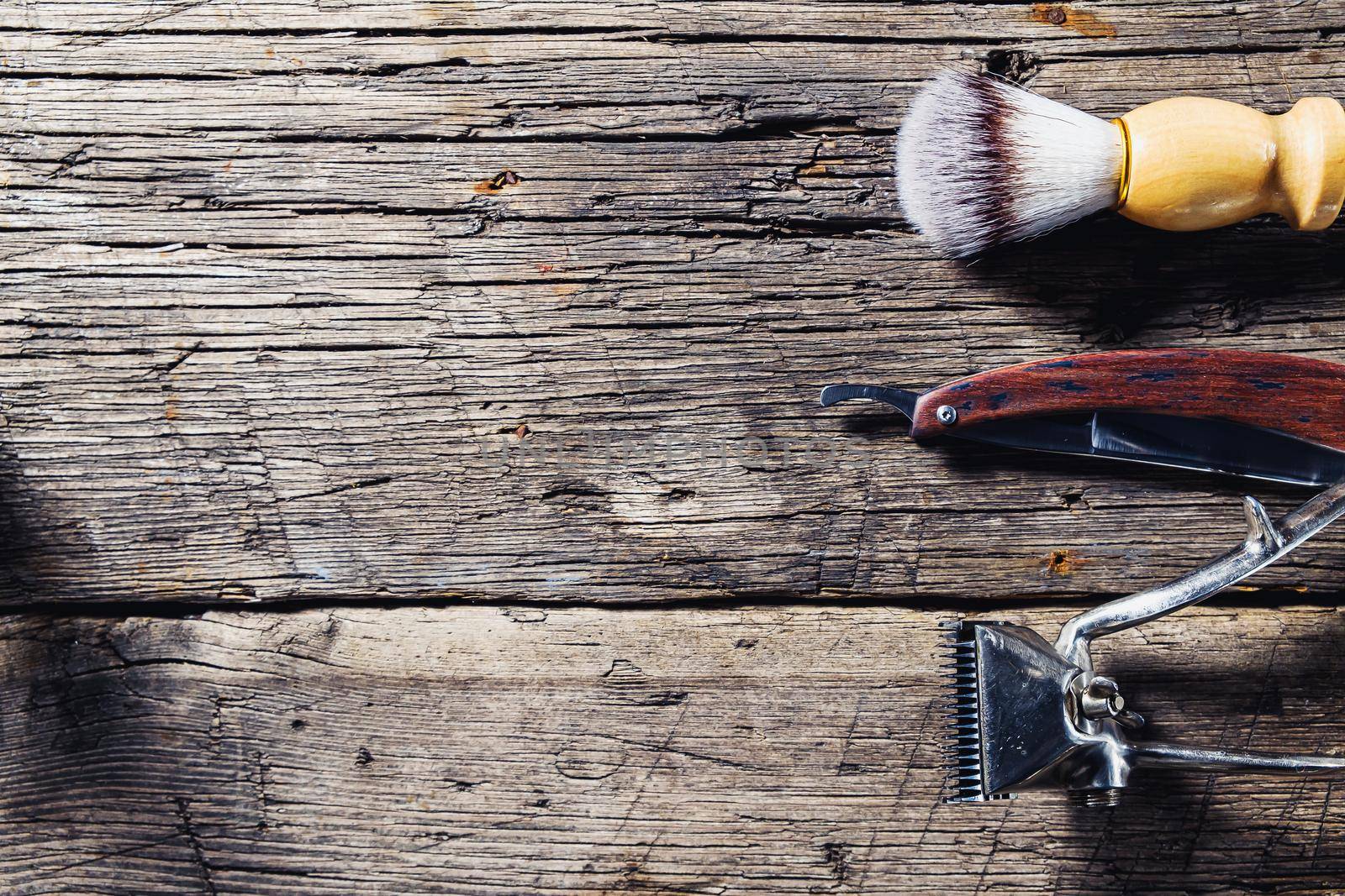 On a rustic wooden weathered surface are old barber tools. Vintage manual hair clipper comb razor shaving brush shaving brush hairdressing scissors. horizontal.