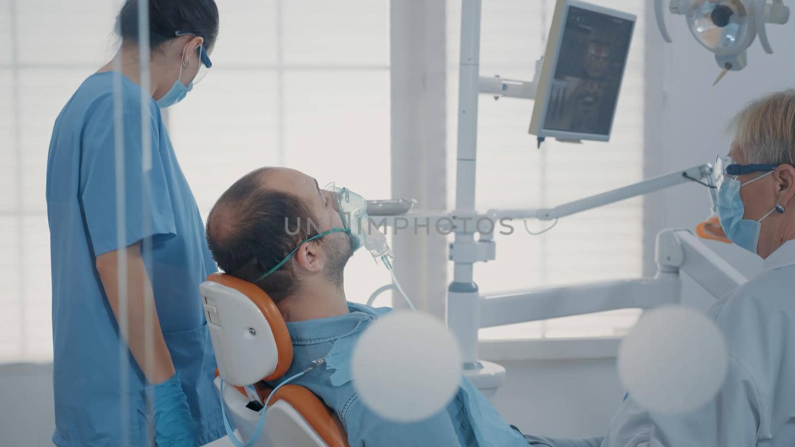 Dental assistant using oxygen mask to do anesthesia on patient before starting surgical procedure at oral care clinic. Nurse giving anesthesic to man, performing stomatological surgery.