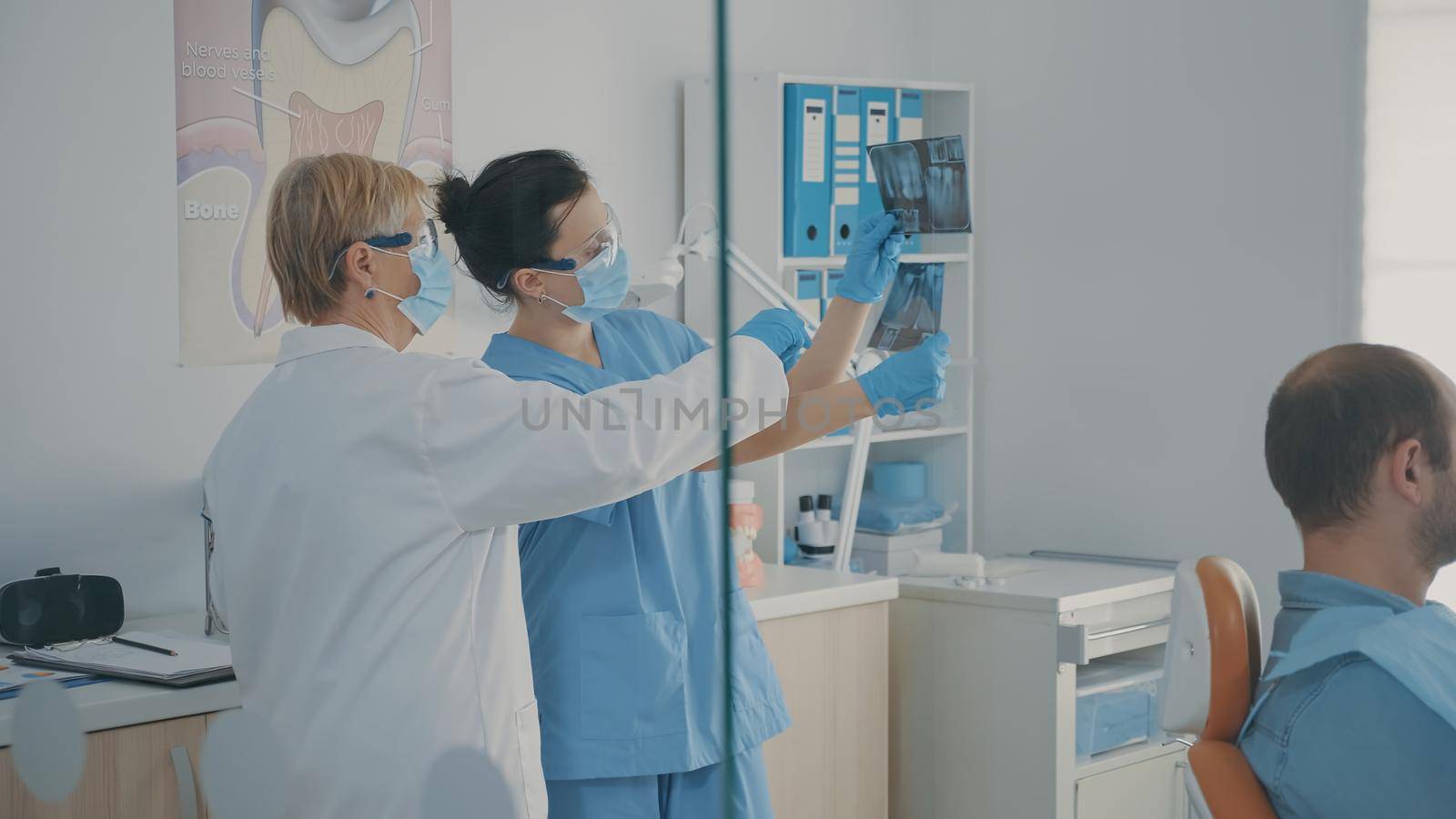 Dentistry team looking at radiography results to do drill procedure on patient in stomatology cabinet. Stomatologist and nurse analyzing teeth x ray scan before dentition surgery.