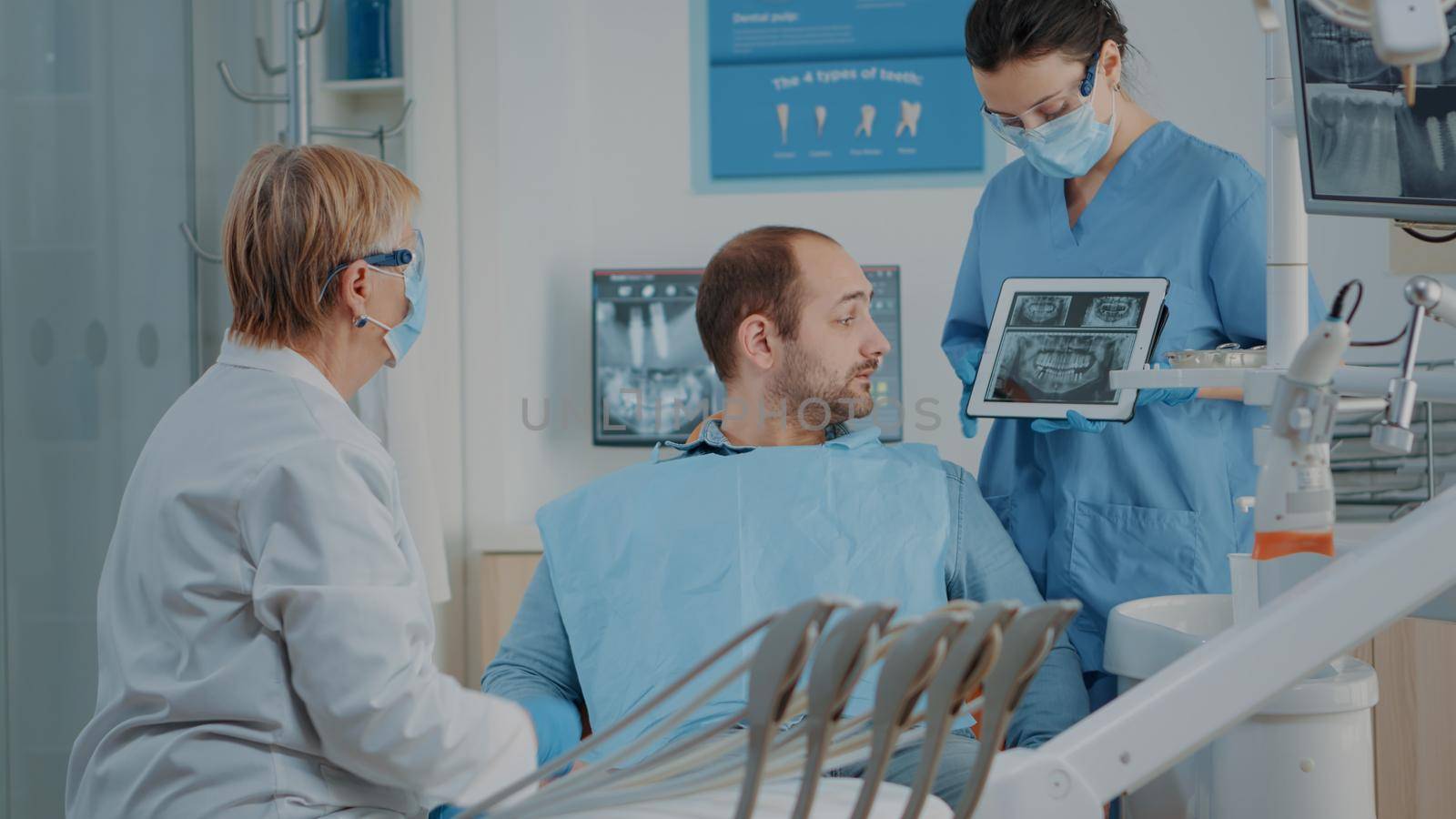 Dentist and nurse showing x ray results to patient with toothache, explaining dental procedure and diagnosis. Stomatology team analyzing radiography to do oral care surgery on man.